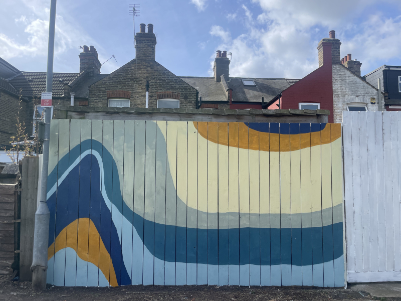 A wooden fence painted with a bright curvy coloured pattern