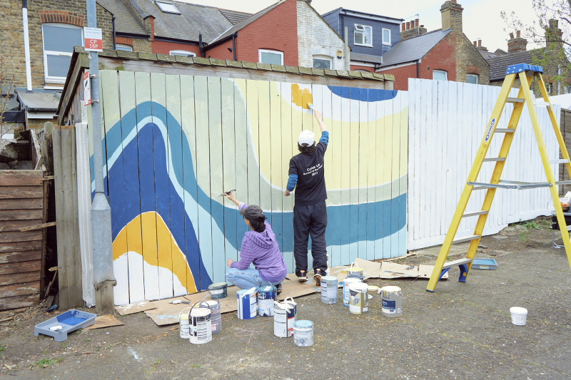 Two people paint a colourful design onto a back fence