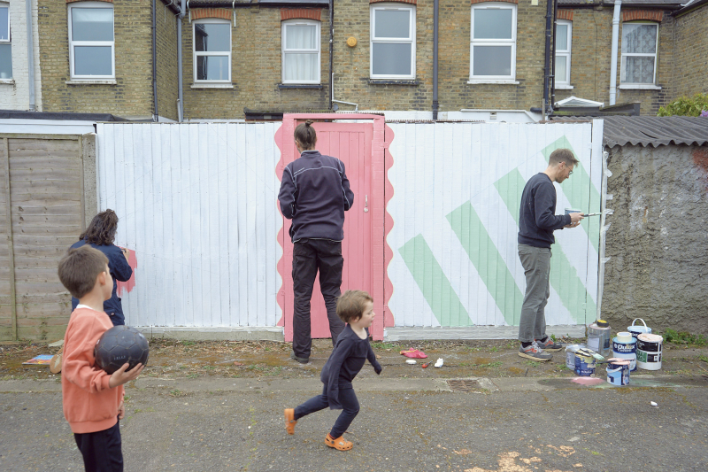 Adults paint a back fence while children play