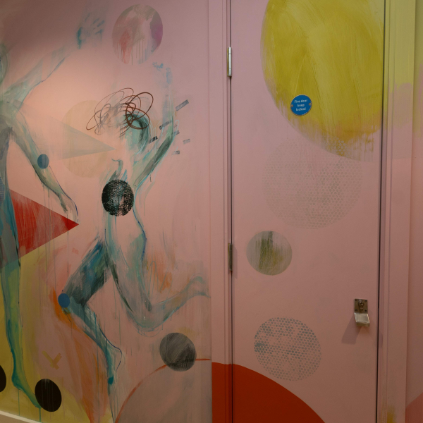 A wall painted in a colourful pink design with coloured spots and two silhouetted figures