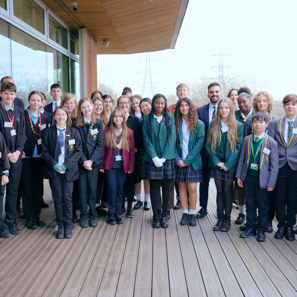 A group of students in school uniforms and a few adults pose for a photo on a wooden deck outside EcoPark House