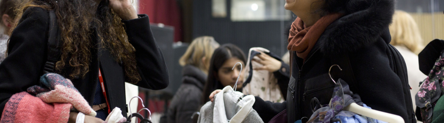 Two young women laughing and holding lots of hangers with clothes on