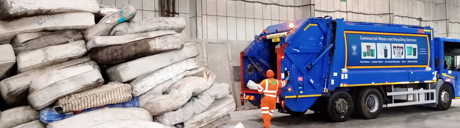 Image of a pile of mattresses inside a warehouse with blue recycling truck