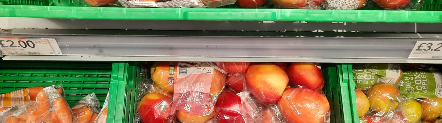 Apples and carrots in plastic packaging on a supermarket shelf