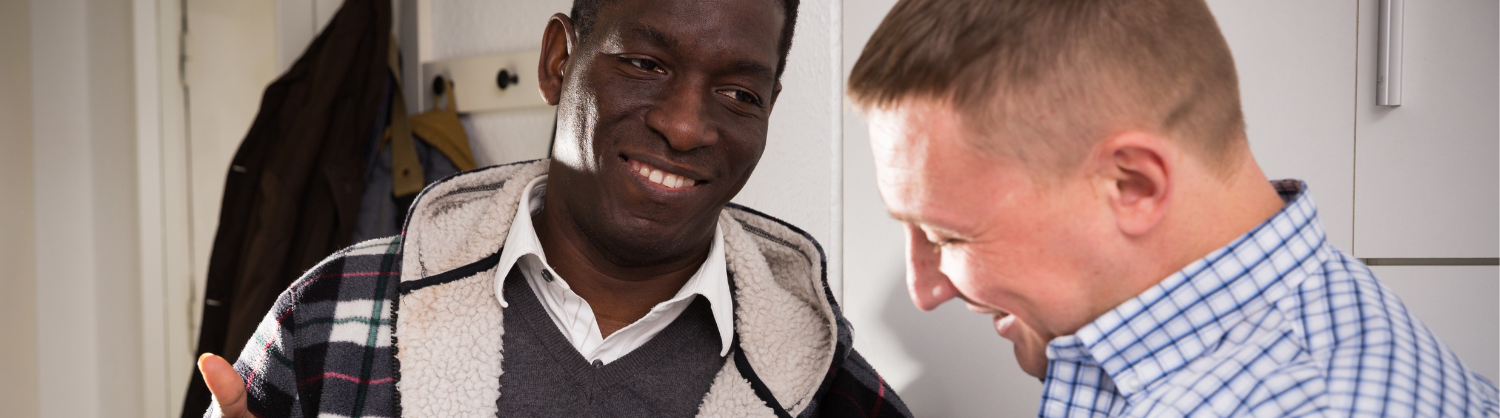 Two men chat while one writes on a sheet of paper