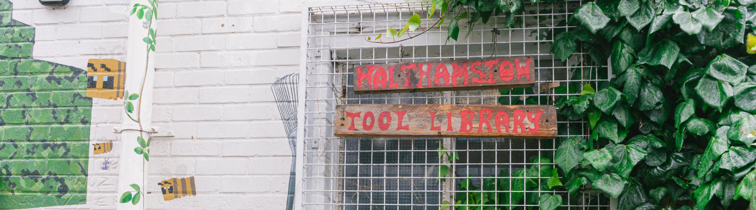 A view of the outer wall of Walthamstow Tool Library, with plants and a sign with its name