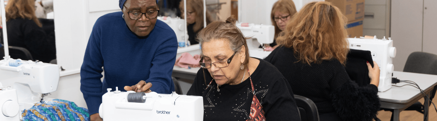 Two ladies leaning over a sewing machine working on a project