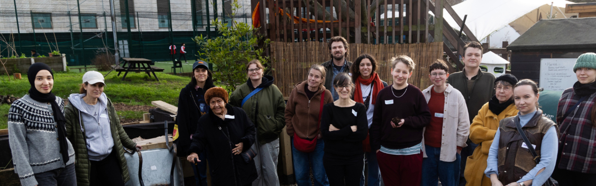 A group of about 20 people stand in a garden allotment posing for the camera