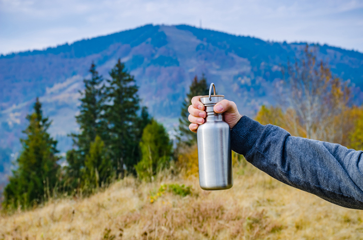 holding reusable water bottle in the forest