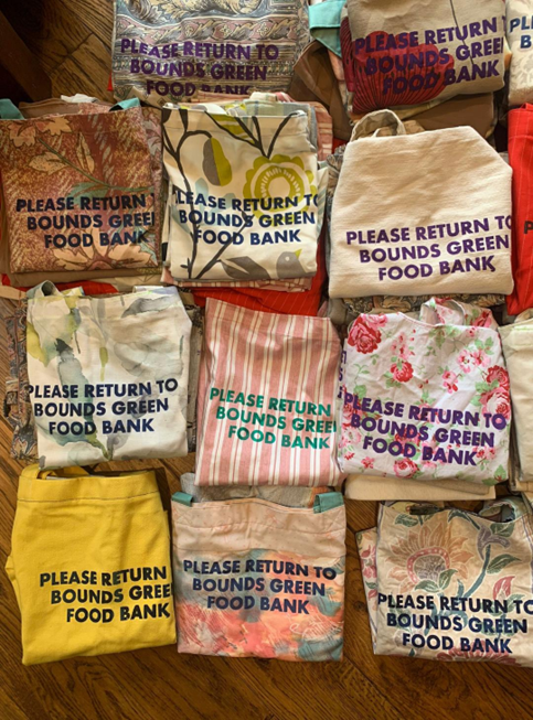 Colourful tote bags with text on them that says 'please return to Bounds Green Food Bank'