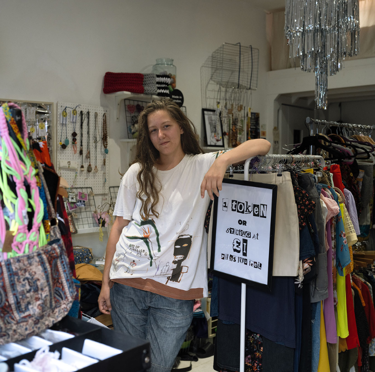 A woman leans on a rack of second-hand clothes