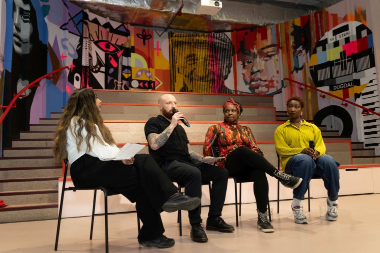 Four people sit on chairs talking in front of a wall mural