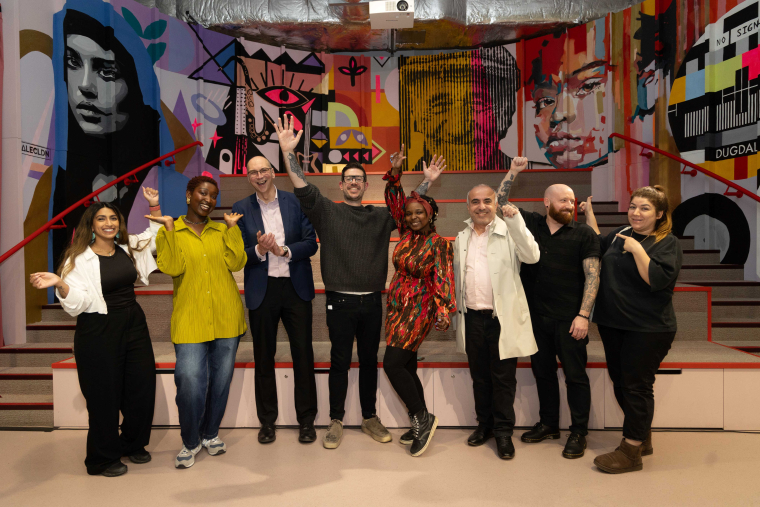 A group of people hold up their hands and smile in front of a wall mural