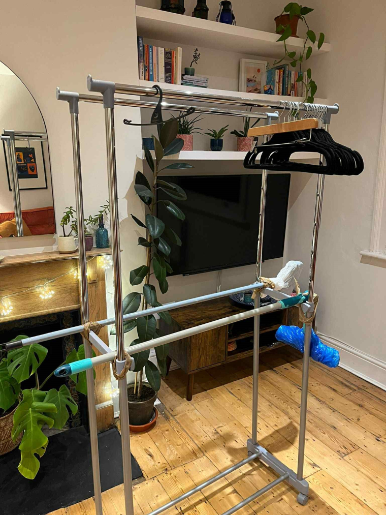Clothes drying rack and brooms being repurposed for hanging space at a clothes swap