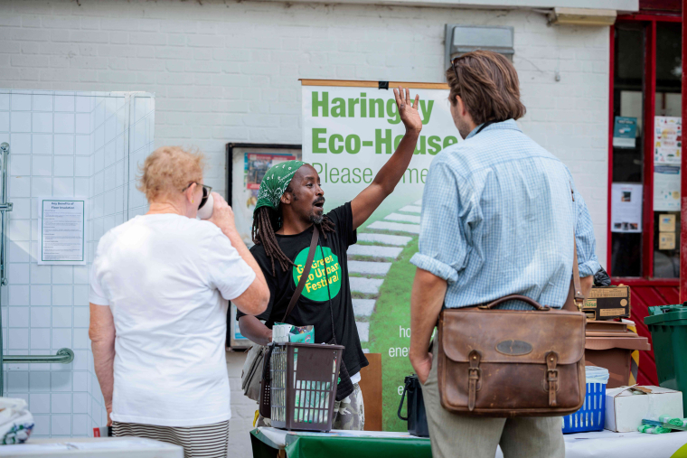 A man in a green bandana gestures to two other people at a festival stall