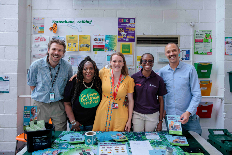 Five people smile at the camera from behind a festival stall