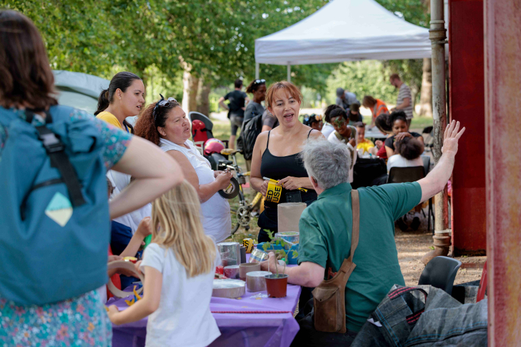 A man sits at a stall with people gathered around chatting