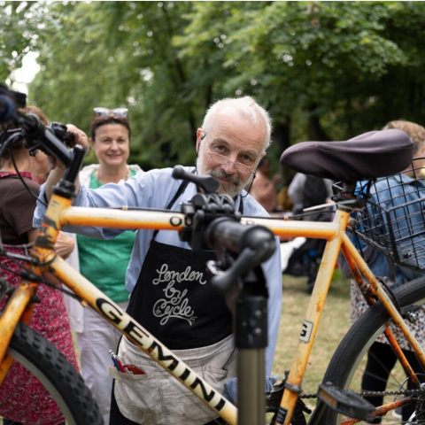 Image of a person standing in a park behind a raised bike smiling at the camera