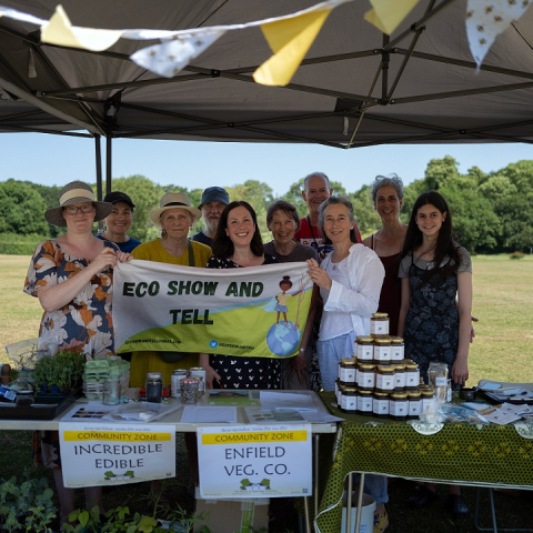 Image of 10 people standing outside in a gazebo holding a banner which reads eco show and tell, smiling at the camera