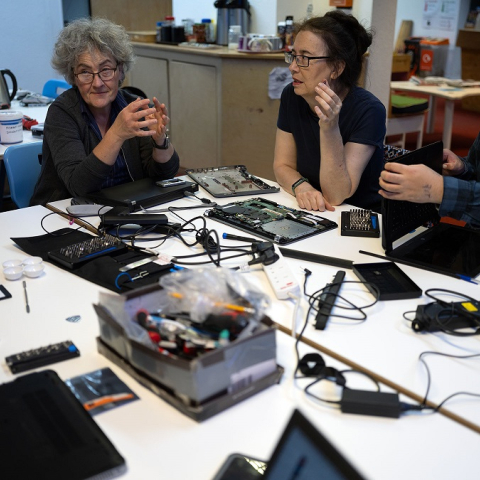Image of four people sitting at table talking and repairing electrical items