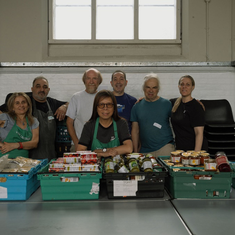 Image of seven people standing behind food trays on a table smiling at the camera