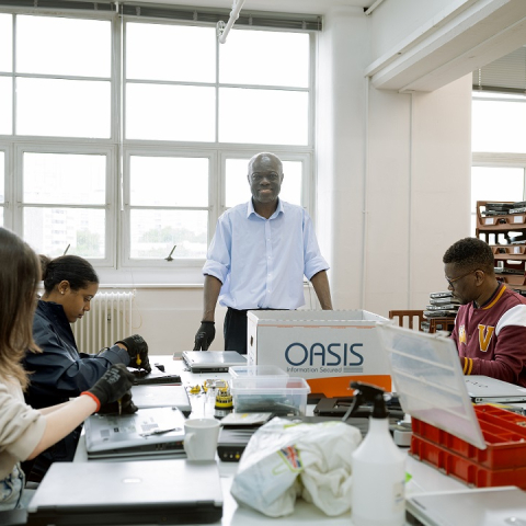 Image of four people working inside computer repair workshop, one person standing smiling at camera