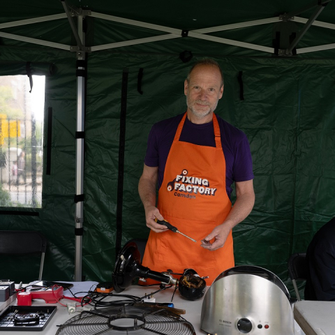 Image of a someone standing inside gazebo wearing Camden Fixing Factory apron, smiling at camera