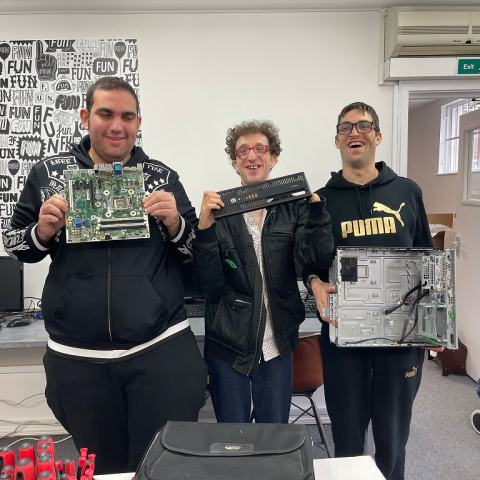 Image of three people standing inside holding computer hardware, smiling at camera