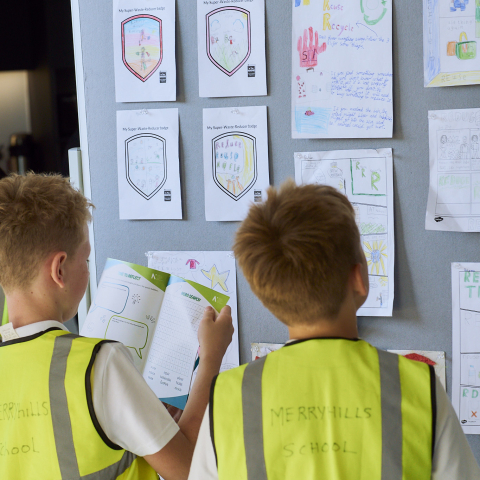 two students in high visibility jackets looking at a pin board
