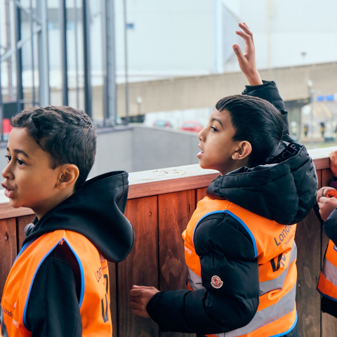 Two students in high visibility jackets on a tour of eco park house one student raising their hand