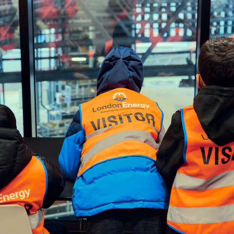 3 students in high visibility jackets looking through a window