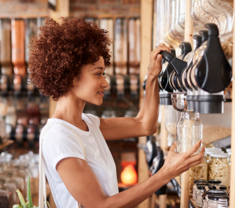 woman wearing white t-shirt filling up a glass jar with cereals from a refill shop