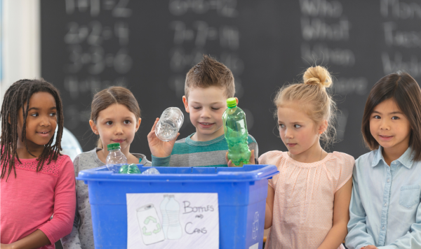 Children placing plastic bottles in a recycling bin